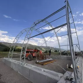 Pilot Buildings steel truss frame being erected on a foundation of precast concrete blocks at an outdoor site.