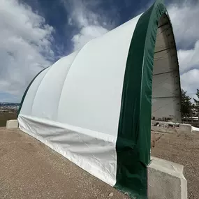 This image provides a side view of a versatile, open-ended fabric building by Pilot Buildings. The structure's durable, two-tone cover is securely mounted on a foundation of pre-cast concrete blocks, showcasing a solid and adaptable installation method. The open endwall reveals the spacious, clear-span interior supported by a robust steel frame, highlighting the easy access for vehicles, equipment, or materials. This design is ideal for accessible storage and operational needs.