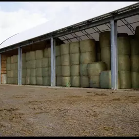 Side profile of a Pilot Buildings structure with straight walls and an open side, filled with large round hay bales for storage.