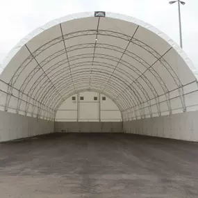 This image displays a finished fabric building by Pilot Buildings, engineered for high-volume storage. The structure is set on tall, solid concrete foundation walls, ideal for containing bulk materials like salt, sand, or agricultural commodities. Its wide, open-front design allows for easy access by heavy machinery, while the clear-span steel truss interior provides a massive, unobstructed space. The bright white fabric cover ensures a well-lit interior, making this a perfect solution for munic