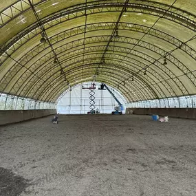 Interior view of a wide-span Pilot Buildings arched structure, configured as an indoor arena, possibly for equestrian use.