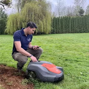 A man kneels on the grass, focused on mowing the lawn with a push mower, surrounded by a lush green landscape.
#lawncare #roboticmowingspecialists