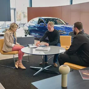 Three people meeting inside Genesis of Milford with a Genesis car in the background