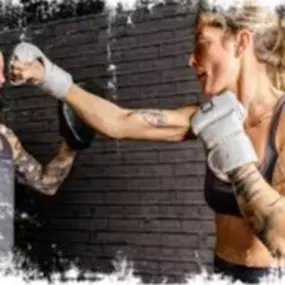 A close-up action shot of a woman practicing boxing techniques with a partner holding pads. She’s wearing open-palm gloves and has a focused expression, highlighting the dynamic and empowering nature of Jabz Boxing workouts.