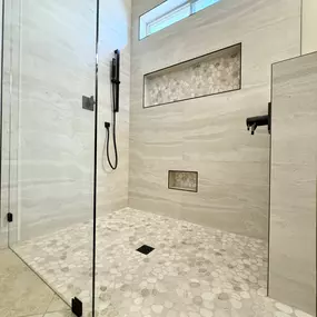 This stunning design features a spacious walk-in shower with sleek glass doors, natural pebble flooring, and stylish built-in niches for functionality and style. Whether you're looking for a complete bathroom remodeling project or a luxurious shower upgrade, Ledezma Remodeling delivers top-tier craftsmanship for your home renovation needs.