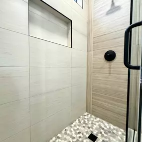 This stunning custom walk-in shower by Ledezma Remodeling showcases a seamless blend of natural textures and modern design. Featuring pebble tile flooring and sleek horizontal wall tiles, it's a perfect example of expert shower remodeling and bathroom renovation. Every detail is crafted to create a serene and functional space.