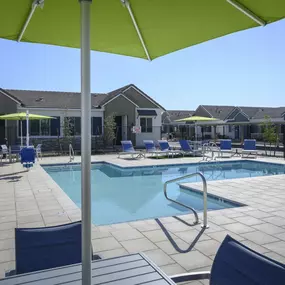 a swimming pool with chairs and umbrellas in front of a house