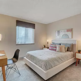 A bedroom with a bed, desk, chair, and window