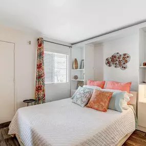 A bedroom with a bed, a window with a curtain, and a wall art
