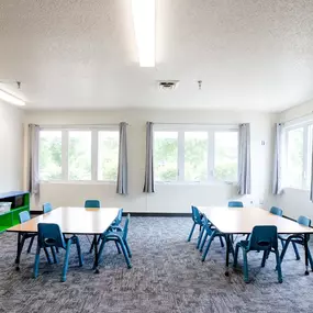 a classroom with tables and chairs and a chalkboard on the wall