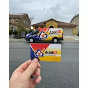 Aced It! Cooling & Heating branded van parked in a residential neighborhood, featuring the company's bold logo with blue, red, and yellow colors. In the foreground, a hand holds a business card showcasing the same logo and vibrant design. The image highlights the professional branding and local HVAC services provided in Corona, CA and surrounding areas. Ideal for showcasing trust, reliability, and visibility in the community.