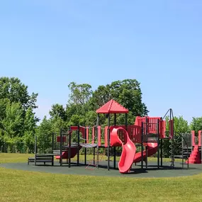 A playground with a red slide and a green lawn