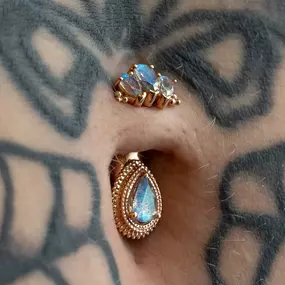 A close-up of a stretched ear piercing with ornate gold and blue gemstone jewelry, including a teardrop-cut blue stone framed in gold beading and a trio of pear-cut stones above.