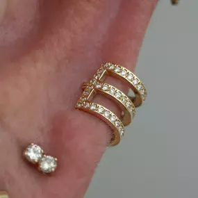 A close-up of an ear with a gold triple-band cuff encrusted with diamonds and a small double diamond stud below it.