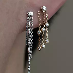 A close-up of mismatched chain earrings: one in silver with angular details and the other in gold with bezel-set diamonds.