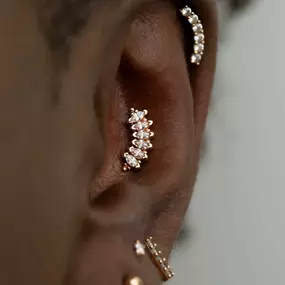 A close-up of an ear with gold and diamond jewelry, including a curved marquise-cut cluster in the conch and a curved diamond row on the helix.