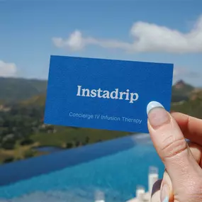 A close-up of a hand with light blue nails holding a blue business card that reads 