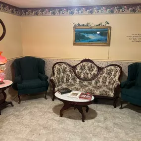 A serene private room at Watts Funeral Homes, furnished with a floral sofa, comfortable chairs, and a warm lamp, offering families a quiet space to gather before funeral services.