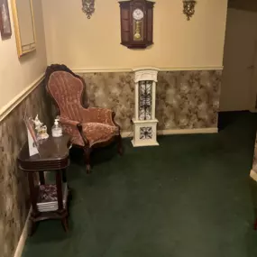 An inviting hallway leading to the restrooms at Watts Funeral Homes, featuring vintage decor, a classic clock, and comfortable seating to ensure guests feel at ease.