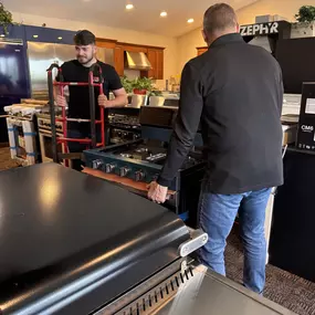 The Voss TV & Appliance team carefully positions a high-end range in their live kitchen showroom setup.