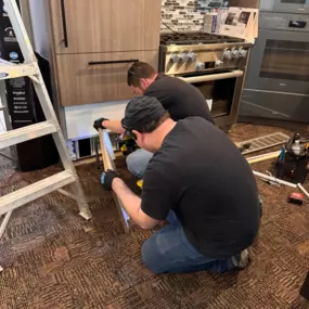 Voss TV & Appliance staff installs custom paneling on a built-in refrigerator to match surrounding cabinetry.