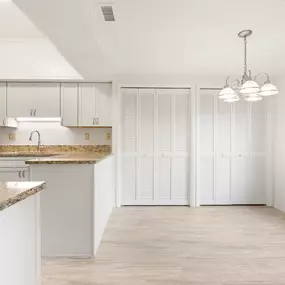 A kitchen with white cabinets and a granite countertop with a dining area