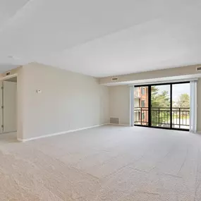 A large living room with a carpeted floor and sliding glass doors leading to a balcony.