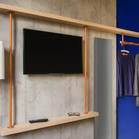 The room at Ibis Budget Amsterdam South features a television mounted on the wall for entertainment, along with a convenient clothes rack for storing personal items. This practical setup provides guests with a comfortable and functional space to relax and stay organized.