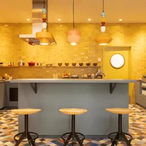 Breakfast area at Adagio Access Brussels Airport with bar stools, colorful lights, and a buffet offering hot and cold options like pastries, bread, fruit, meat, and yogurt.