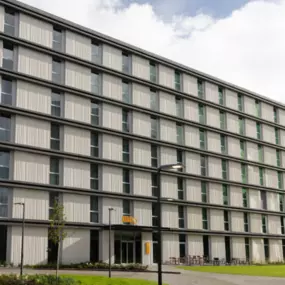 Exterior of Adagio Access Brussels Airport, a modern multi-story hotel with large windows, surrounded by greenery and outdoor seating, located near Brussels Airport.