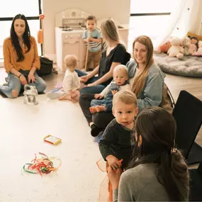 Moms and their toddlers sit at a table smiling and talking