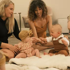 Two babies play together with their moms' support