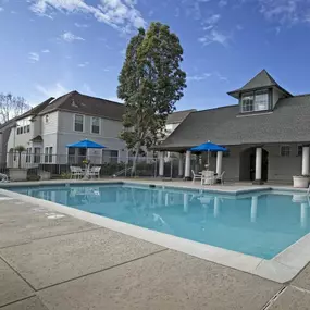 A swimming pool surrounded by a concrete patio and a house with a pool house.