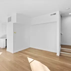 A white room with wooden flooring and a staircase on the right side.
