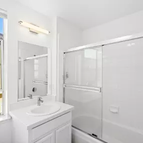 A white bathroom with a sink, mirror, and shower