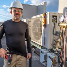 Certified HVAC technician performing maintenance on a commercial rooftop air conditioning unit. Equipped with professional tools, including pressure gauges and a power drill, ensuring optimal system performance. MAX Comfort HVAC provides expert HVAC installation, repair, and maintenance services in Allentown, PA, delivering high-quality solutions for residential and commercial buildings.