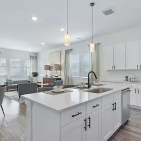 A modern open-concept kitchen and living space featuring white cabinetry, stainless steel appliances, and elegant pendant lighting.