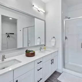 Bathroom featuring a double vanity with white cabinetry and black hardware, a large mirror, and a glass-enclosed walk-in shower.