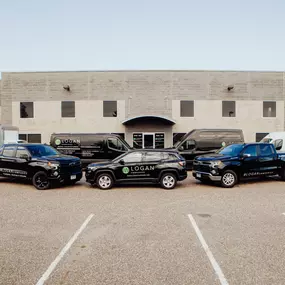 A fleet of branded Logan Companies vehicles, including trucks, vans, and a box truck, parked in front of a commercial building.