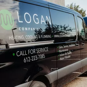 A black Logan Companies service van with detailed branding and service offerings, including heating, cooling, and plumbing