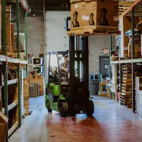 A Logan Companies employee operating a green forklift inside a warehouse, moving HVAC equipment.