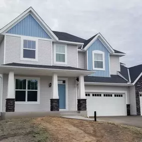 Newly built home with fresh roof gutter installation. Notice the white gutters and downspouts contrasting against the light gray siding and blue accents, ensuring efficient water drainage.