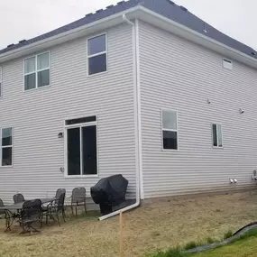 Rear view of a home showcasing newly installed white gutters and downspouts. Notice the continuous lines along the roof edge, efficiently channeling rainwater away from the foundation and landscaping.