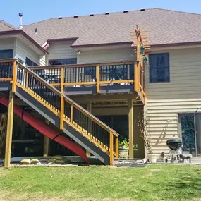 A house with a sloped roof and a newly built elevated deck with stairs. The gutter system runs along the roof edge, directing rainwater away. The gutter appears well-maintained, complementing the home's exterior while protecting against water damage