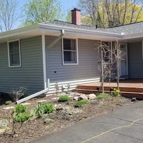 The photo features a single-story house with a clean, well-maintained roof gutter system. The white gutters run along the roofline, with downspouts effectively directing water away from the foundation, ensuring proper drainage and protection for the home.