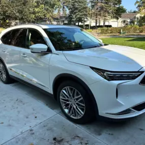 A white Acura MDX with a flawless finish after our full-service auto detailing, including interior cleaning and exterior polishing, parked on a residential driveway.