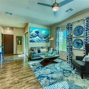 A living area of an apartment with wood floors with a blue patterned rug and a ceiling fan