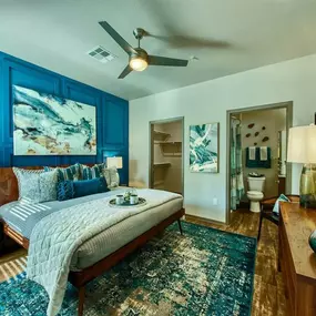 A bedroom with queen size bed and blue accent colored wall behind it. A door leads to the a bathroom and a second door shows the walk-in closet.