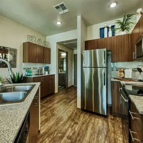 A kitchen with stainless steel double sink and stainless steel refrigerator.  Beautiful modern cabinets line kitchen walls and surround black range.