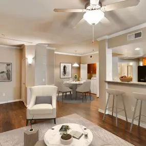 A living area with a ceiling fan, light beige carpet, wood flooring, and white furniture